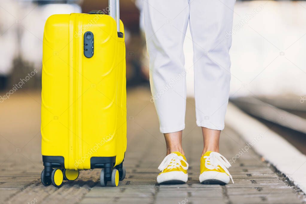 woman with yellow suitcase on wheels walking by railway station copy space