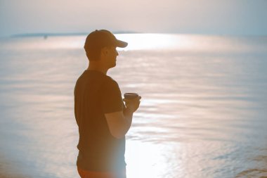 Deniz kıyısında su içinde yürüyen, seyahat kupalı bir adam. yaz zamanı