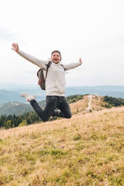 Sırt çantalı adam dağ yürüyüşü konseptinde zirvede zıplamaktan mutlu.