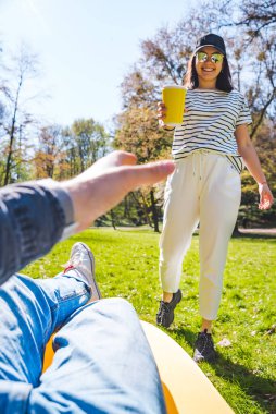 Kamu parkındaki kanepede uzanmış bir adam elinde çay fotokopisi olan bir kağıt bardak tutuyor.