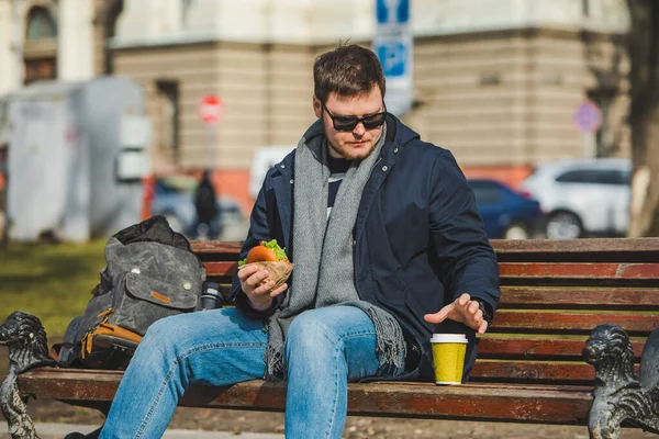 Junger Lächelnder Mann Der Burger Isst Und Kaffee Trinkt Sitzt — Stockfoto