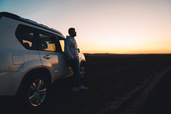 man standing near white suv car looking at sunset copy space