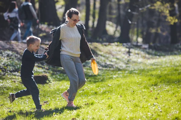 Mother with sun playing frisbee at spring sunny park — Stock Photo, Image