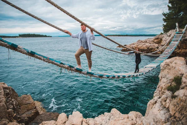 Casal mulher com homem andando por ponte de suspensão instável cruzando baía do mar — Fotografia de Stock