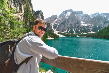 Sırt çantalı genç ve güçlü bir adam dağlarda göle bakıyor. Boşluğu kopyala