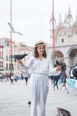 Beyaz şapkalı kadın Venice City Meydanı San Marco 'da güvercinlerle eğleniyor.