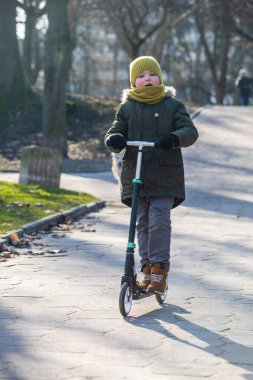 Küçük çocuk, şehir parkında scooter kullanıyor. Açık hava aktiviteleri