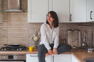 sarı çay bardağı ile mutfak masasında oturan gülümseyen güzel kadın. ev hanımı kavramı