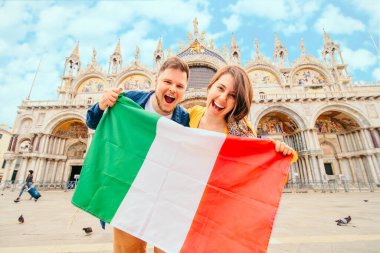 İtalya, Venedik 'te Aziz Marks Bazilikası' nın önünde İtalyan bayrağı tutan genç adam ve kadın. Yazın ünlü seyahat simgesi