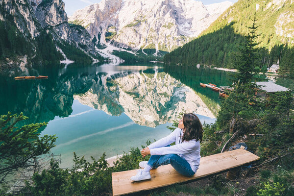 woman sitting on the bench looking at pragser wildsee in north italy. copy space. summer vacation
