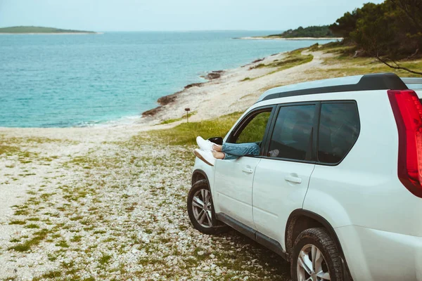 Frauenbeine ragen aus Auto, das am Meeresstrand geparkt ist — Stockfoto