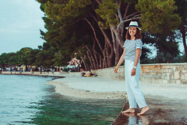 Donna in abiti bianchi e cappello fedora passeggiando sulla spiaggia di mare — Foto Stock