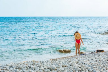 Yaz tatili için deniz kenarında hasır şapkalı genç ve güzel bir kadın. Kırmızı mayo.