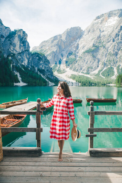 woman in red sundress sitting on wooden stairs looking at lake in mountains. travel concept