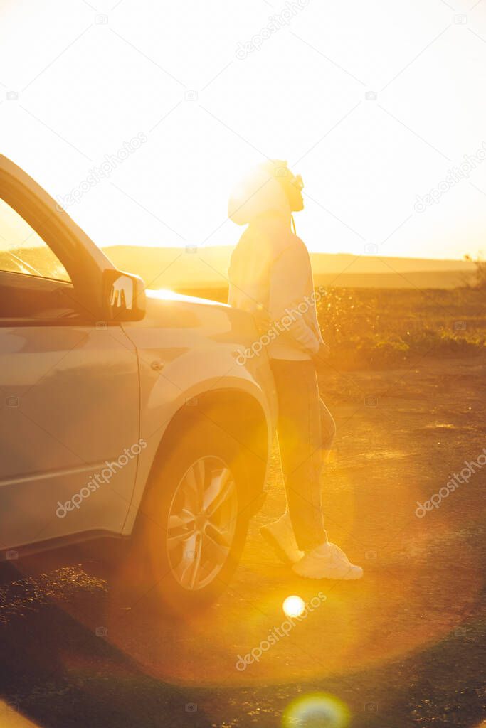 woman enjoying of sunset ar countryside. standing near white SUV. road trip