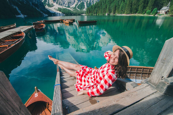 woman in red sundress sitting on wooden stairs looking at lake in mountains. summer vacation