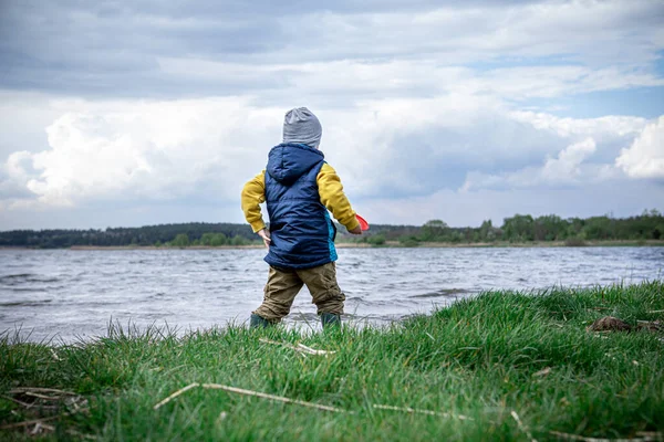 little kid throwing rocks in lake. rubber boots. copy space