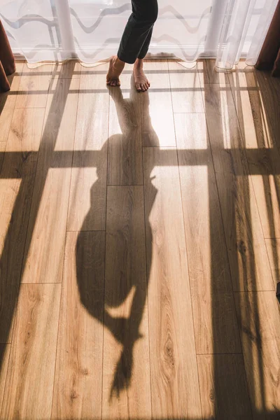 harsh shadow of woman on room floor. light in window