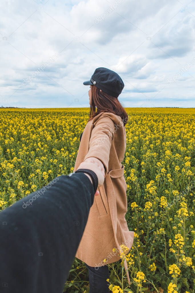 follow me concept woman holding man hand leading to yellow rapeseed field. copy space