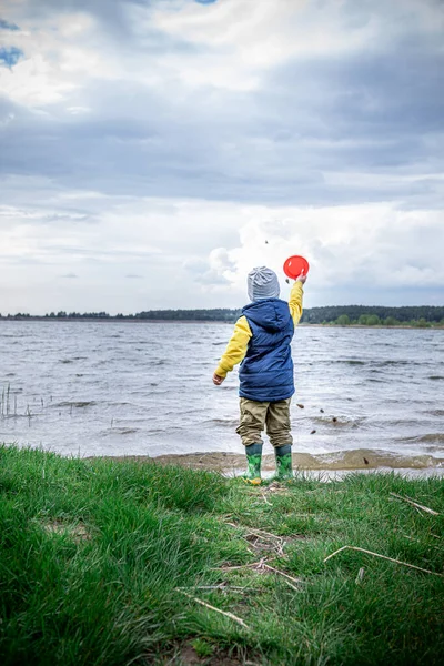 little kid throwing rocks in lake. rubber boots. copy space