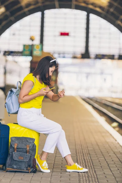 Улыбающаяся Красивая Женщина Сидящая Желтом Чемодане Колесами Железнодорожном Вокзале — стоковое фото