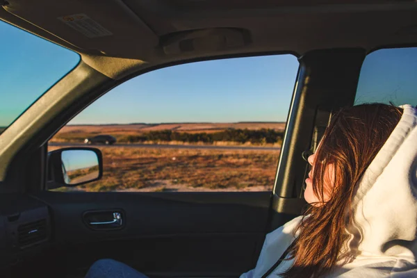 女性は車の中で道路を見て座っている 日没の時間だ 乱雑な髪 — ストック写真
