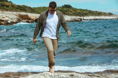 Rüzgarlı yaz tatilinde Rocky Beach 'te yürüyen bir adam. Deniz manzarasının tadını çıkar. yaz zamanı