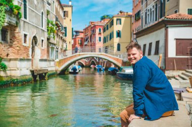 Venedik Kanalı 'nın yanındaki gölde oturan adam gülümsüyor ve fotokopi alanına bakıyor.