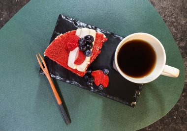 Siyah tabakta çilekli kek ve kahve.