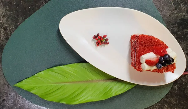 Beyaz tabakta çilekli pasta ve büyük yaprak.