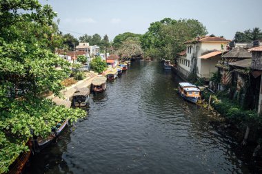 Alappuzha 'daki ana su kanalı Alleppey, Kerala, Hindistan' da kanal boyunca tekne, ev ve ağaçlarla dolu.
