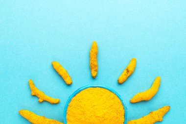 Mavi kasede zerdeçal tozu ve mavi arkaplanda güneş şeklinde kuru kökler..