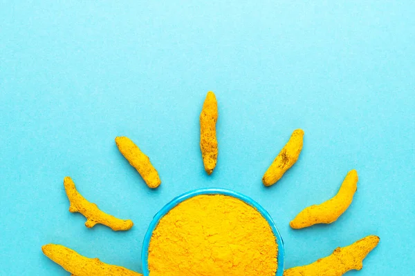 Mavi kasede zerdeçal tozu ve mavi arkaplanda güneş şeklinde kuru kökler..