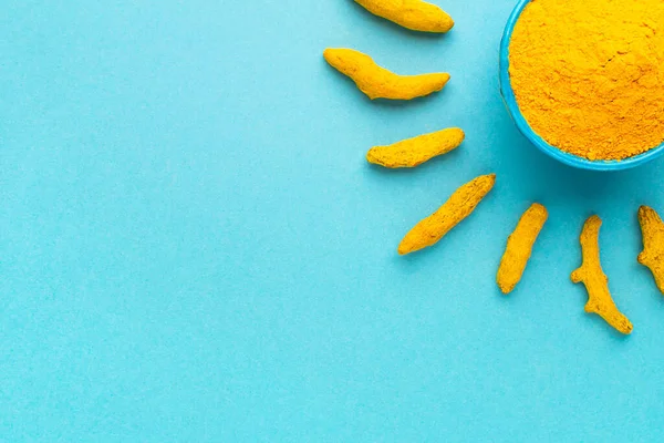 Mavi kasede zerdeçal tozu ve mavi arkaplanda güneş şeklinde kuru kökler..