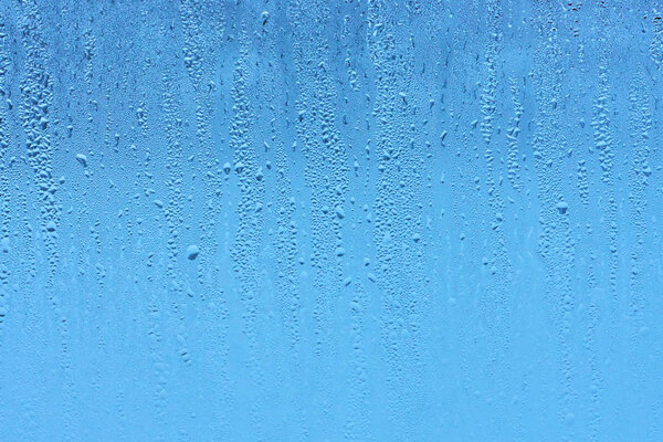 Window glass with condensation high humidity , large droplets flow down , cold tone. Natural water drop background