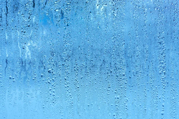 Window glass with condensation high humidity , large droplets flow down , cold tone. Natural water drop background