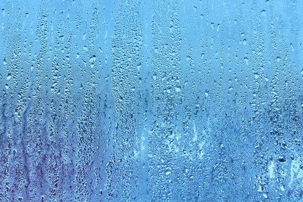 Window glass with condensation high humidity , large droplets flow down , cold tone. Natural water drop background