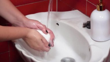 Yaygın enfeksiyon riskini azaltmak için sabunla etkili el yıkama. Banyo lavabosundaki kadın, akan suyla, beyaz sabun çubuğuyla ellerini ovuşturuyor ve bakterileri öldürmek için iyi yıkama tekniği uyguluyor..