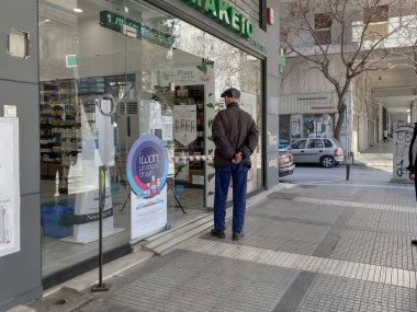 Selanik, Yunanistan - 16 Mart 2020: Coronavirüs tedbirleri iş ve günlük yaşamı etkiliyor. Yunan büyükleri, Yunan hükümetinin COVID-19 'u önleme kararı doğrultusunda eczanenin dışındaki mesafesini koruyorlar.
