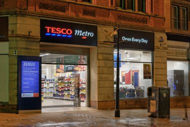 Manchester, İngiltere - 20 Şubat 2020: İngiliz Tesco Metro süpermarket perakende satış mağazası girişi. Şehir merkezindeki 58-66 Market Caddesi 'ndeki bakkaliye ve genel ürünler süpermarketinin dış gece görüntüsü.