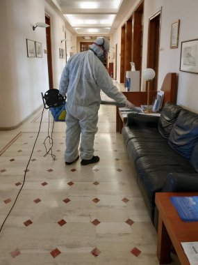 Selanik, Yunanistan - 19 Mart 2020: Koruyucu üniformalı işçi iç uzaya dezenfektan püskürttü. Tam vücut giysili bir erkek COVID-19 Coronavirus 'a karşı dezenfeksiyon uygular..