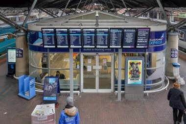 Manchester İngiltere havaalanı tren istasyonu ön cephede bekliyor. Demiryolu rayları etrafındaki açık büfe binasının dış görünümü MAN havaalanı alanındaki bağlantı bilgilerini aşırı ekran ile birlikte.