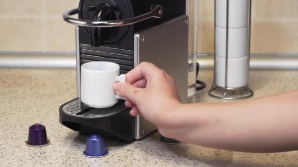 Création d'espresso sur une machine automatique à l'aide de capsules en aluminium. Femme à évier de cuisine ajoute une gousse sur le dessus de la cafetière et fait chaud café goutte à goutte avec de la crème riche sur une tasse blanche .