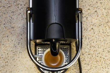 Otomatik bir makinede alüminyum kapsüller kullanarak espresso yaratmak. Üzerinde beyaz bir fincanla kahve makinesi olan mutfak tezgahı, kremalı sıcak kahve yapmak için kullanılır..