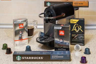 Automatic Nespresso machine used to create aluminum capsules espresso. Starbucks, Illy and LOR metal colorful pods around coffeemaker, for making dripping coffee. clipart
