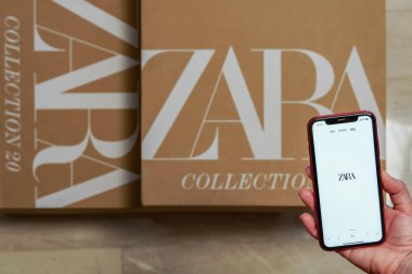Zara İspanyol giysileri ve aksesuarları çevrimiçi dağıtım kutusu. Inditex 'in sahibi olduğu perakende koleksiyonu web sayfasında akıllı telefon kullanan bir kadın. Üzerinde şirket logosu olan sipariş paketi var..