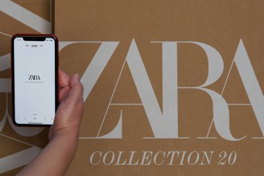 Zara İspanyol giysileri ve aksesuarları çevrimiçi dağıtım kutusu. Inditex 'in sahibi olduğu perakende koleksiyonu web sayfasında akıllı telefon kullanan bir kadın. Üzerinde şirket logosu olan sipariş paketi var..
