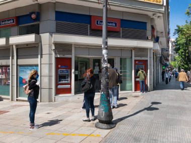Selanik ve Yunanistan Coronavirüs tedbirleri iş ve günlük yaşamı etkiler. Maske takan Yunanlılar, hükümetin COVID-19 'u önleme kararı doğrultusunda bankanın dışında mesafelerini koruyorlar.