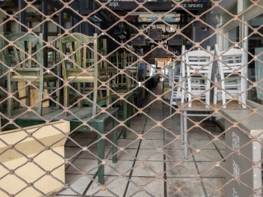 Selanik ve Yunanistan 'ın kapalı alandaki boş oturma restoranları işi etkiliyor. COVID-19 hükümet önlemleri gıda hizmetlerini etkilerken, Modiano Market 'te istiflenmiş sandalye ve masaların bulunduğu kapalı meyhaneler