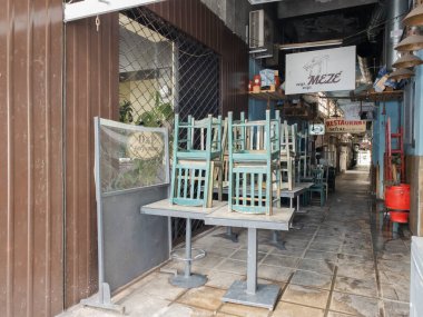 Selanik ve Yunanistan 'ın kapalı alandaki boş oturma restoranları işi etkiliyor. COVID-19 hükümet önlemleri gıda hizmetlerini etkilerken, Modiano Market 'te istiflenmiş sandalye ve masaların bulunduğu kapalı meyhaneler